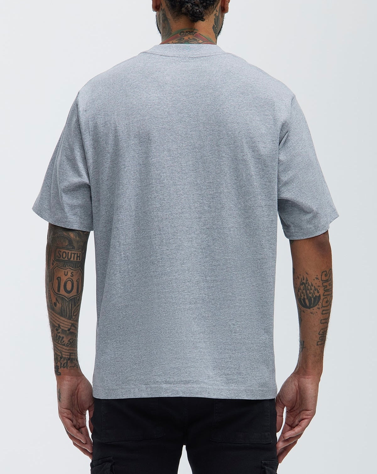 Person wearing a gray t-shirt with tattoos visible on arms against a white background